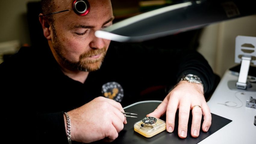 A skilled watchmaker focuses on repairing a watch with precision tools under a lamp.